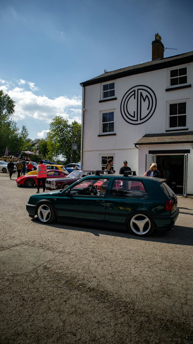 People gather around classic cars parked at an outdoor event.