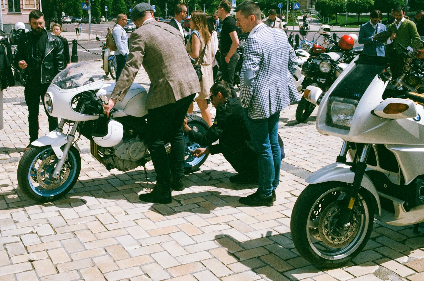 People examine and discuss motorcycles at an outdoor gathering.